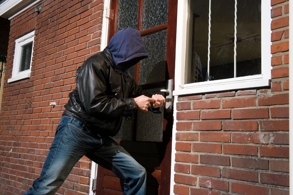 Burglar trying to get into a house by the backdoor (Do Home Security Systems Reduce Burglaries )